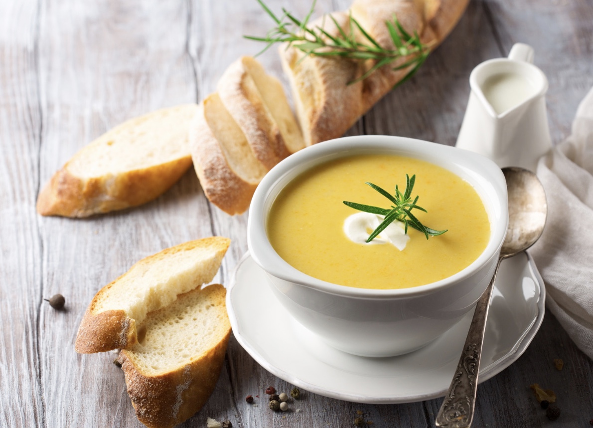 A bowl of creamy soup with fresh bread and rosemary