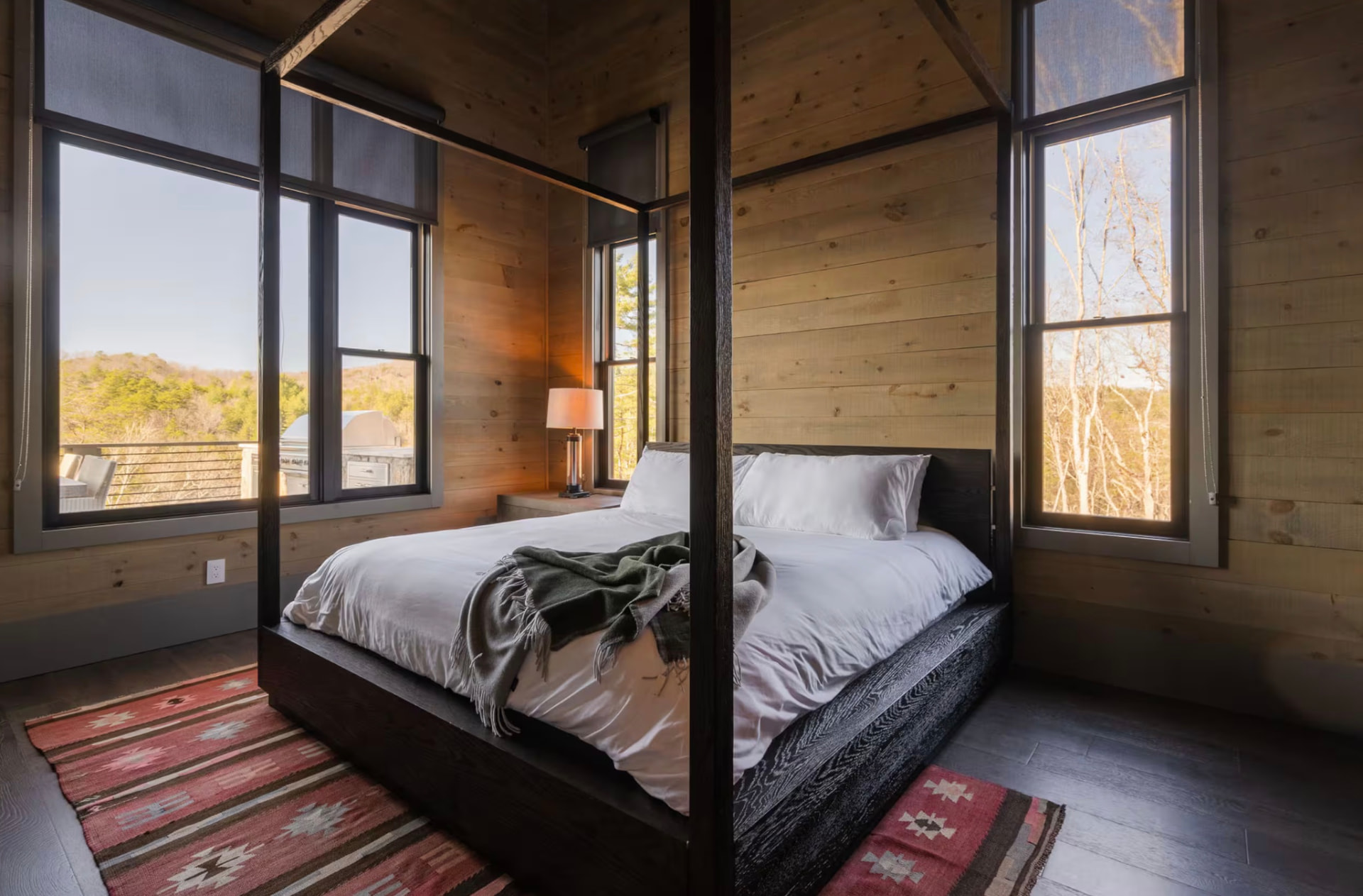 King bedroom with a dark four-poster bed, pine walls, and windows on three sides
