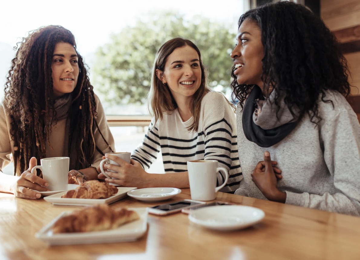 Three women laughing together over coffee and pastries