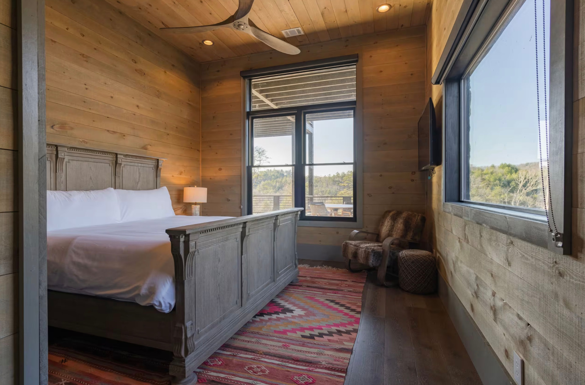King bedroom with a carved wooden bed frame, kilim rug, and a cozy reading chair